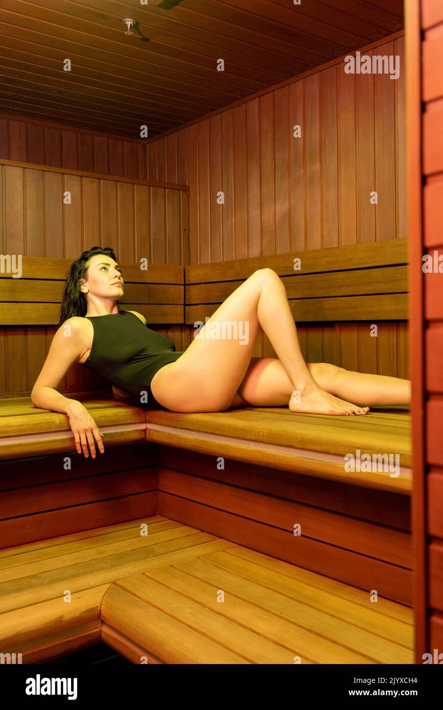Beautiful adult woman in black swimsuit rests in finnish sauna, having spa procedures at luxury resort Stock Photo