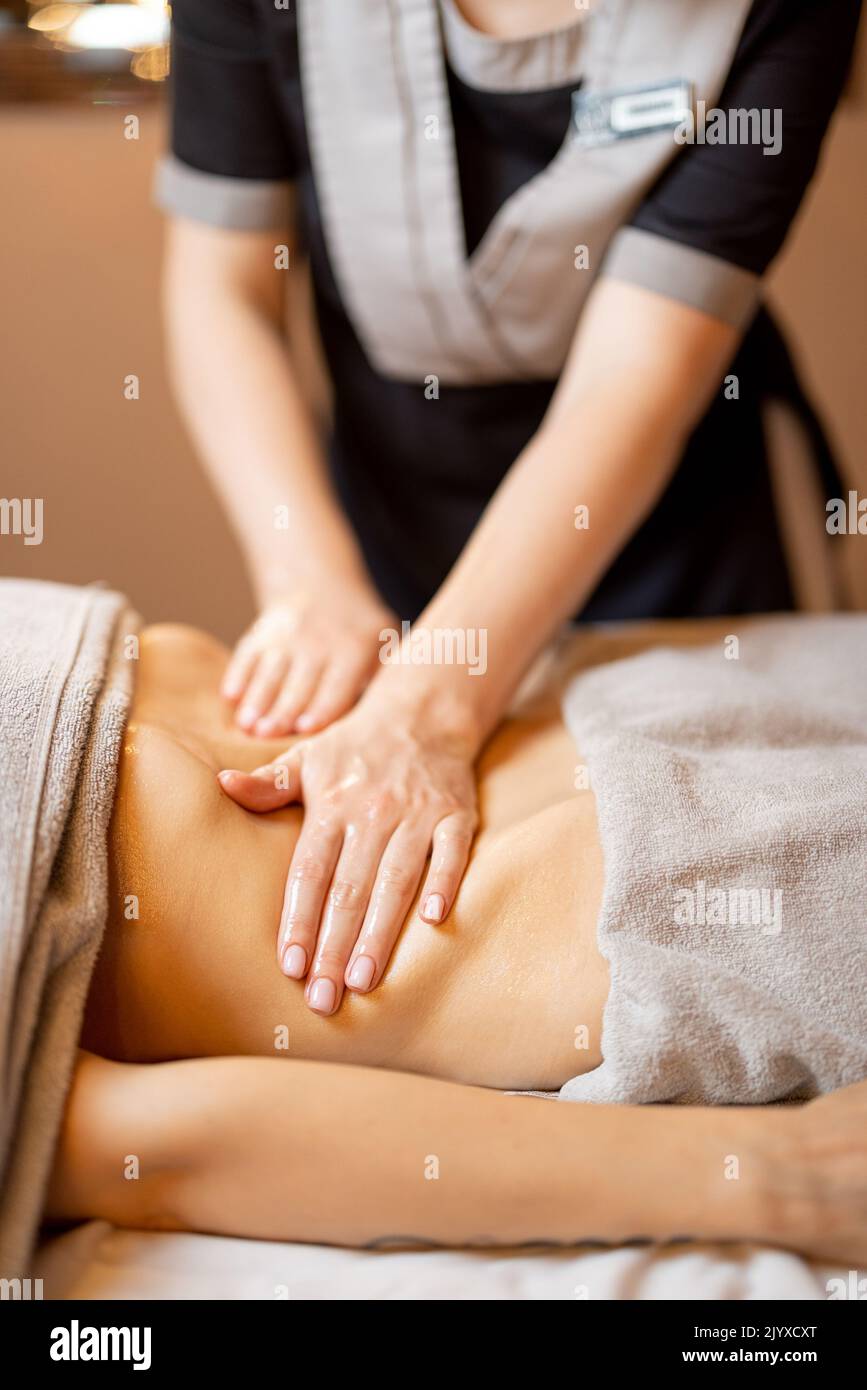 Masseuse performs professional abdominal massage for female client lying on a couch, close-up on hands Stock Photo