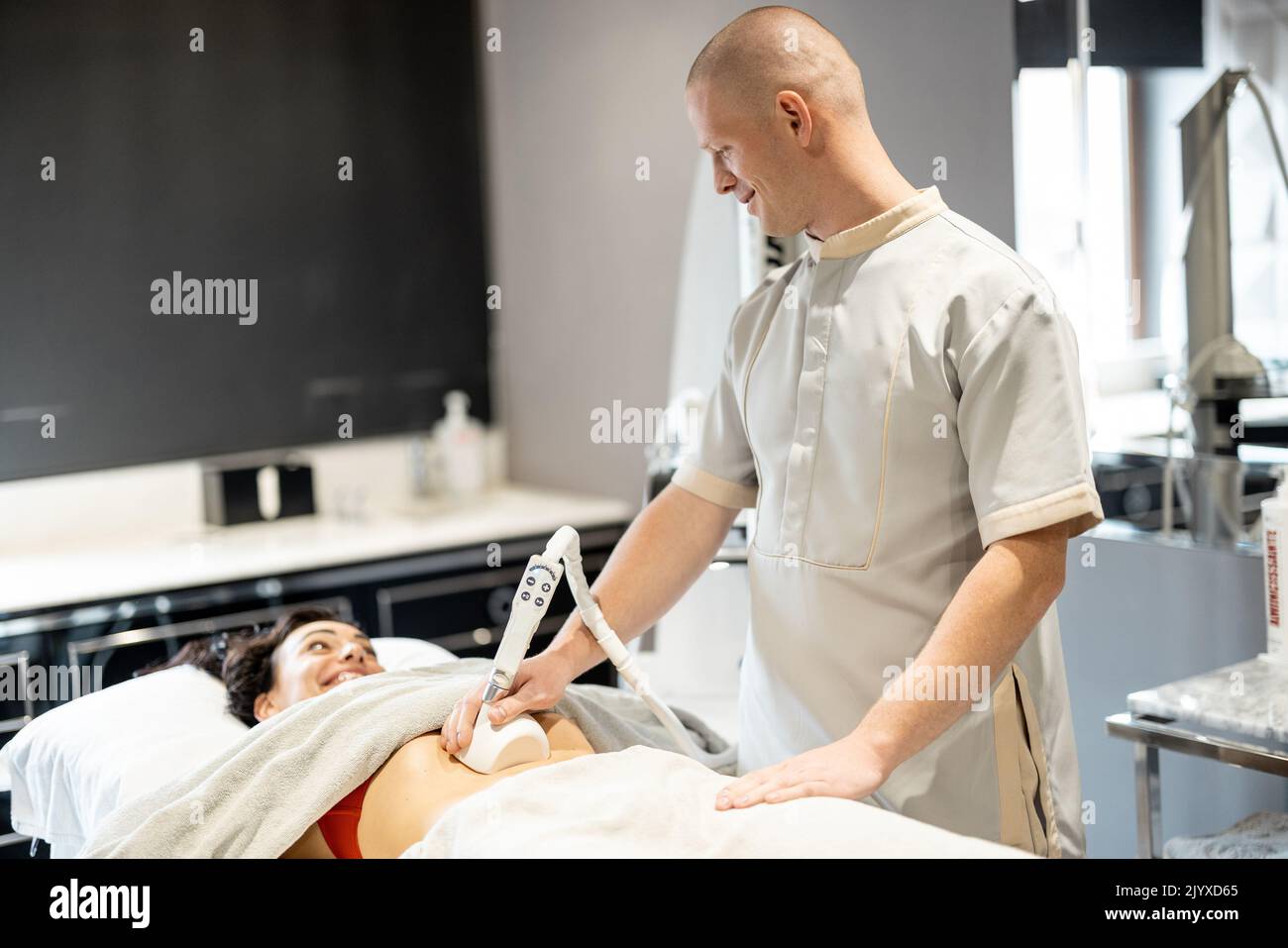 Employee of the medical center applying vacuum roller massage for client's belly area at beauty salon. Concept of modern medical procedures for beauty Stock Photo