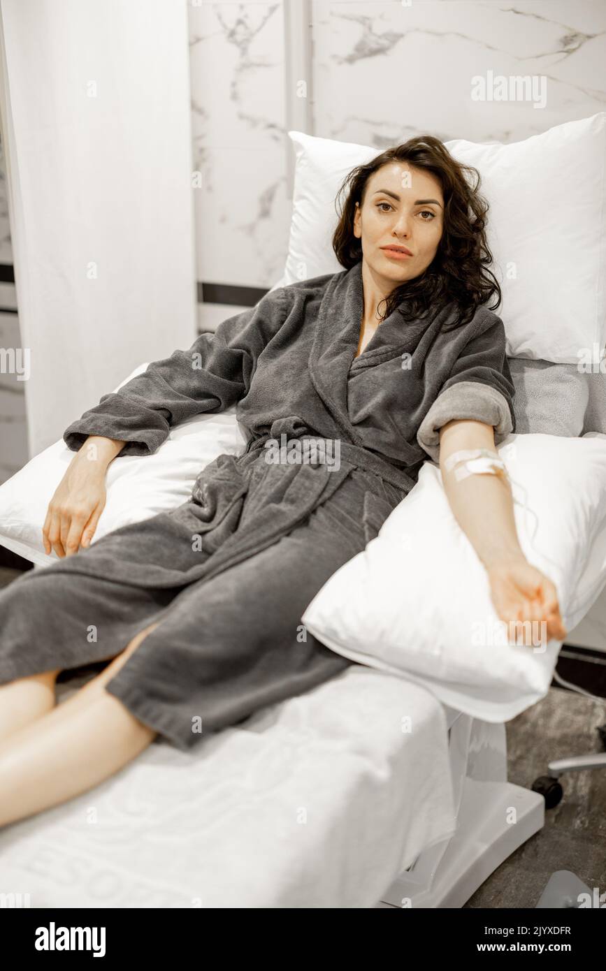 Happy woman in bathrobe lying on medical couch during blood wash procedure with catheter on her arm at medical centre Stock Photo