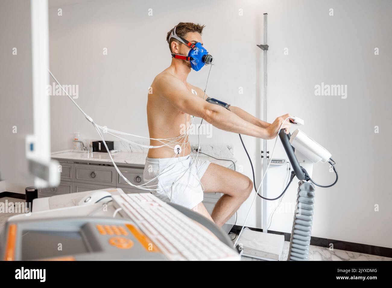 Man athlete with breath mask and electrodes training on bike simulator, examining his cardiovascular system at medical office Stock Photo