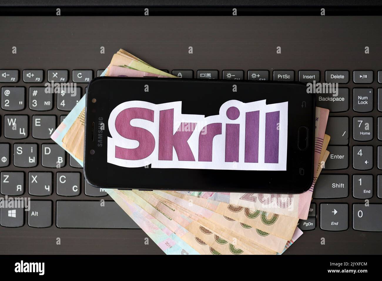 TERNOPIL, UKRAINE - SEPTEMBER 6, 2022 Skrill paper logotype lies on black laptop keyboard with ukrainian hryvnia bills. Payoneer is American financial Stock Photo