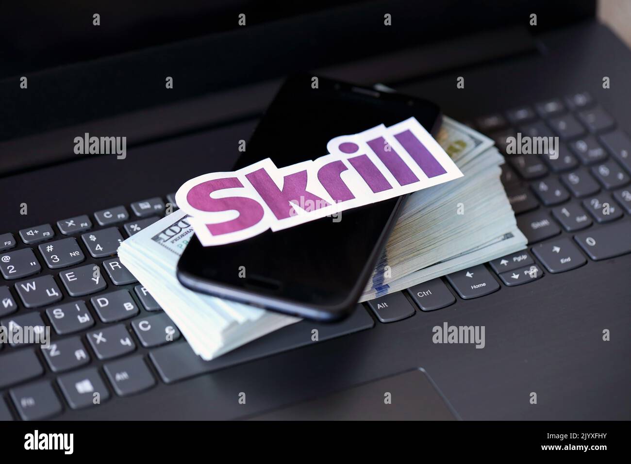 TERNOPIL, UKRAINE - SEPTEMBER 6, 2022 Skrill paper logotype lies on black laptop keyboard with US dollar bills. Payoneer is American financial service Stock Photo