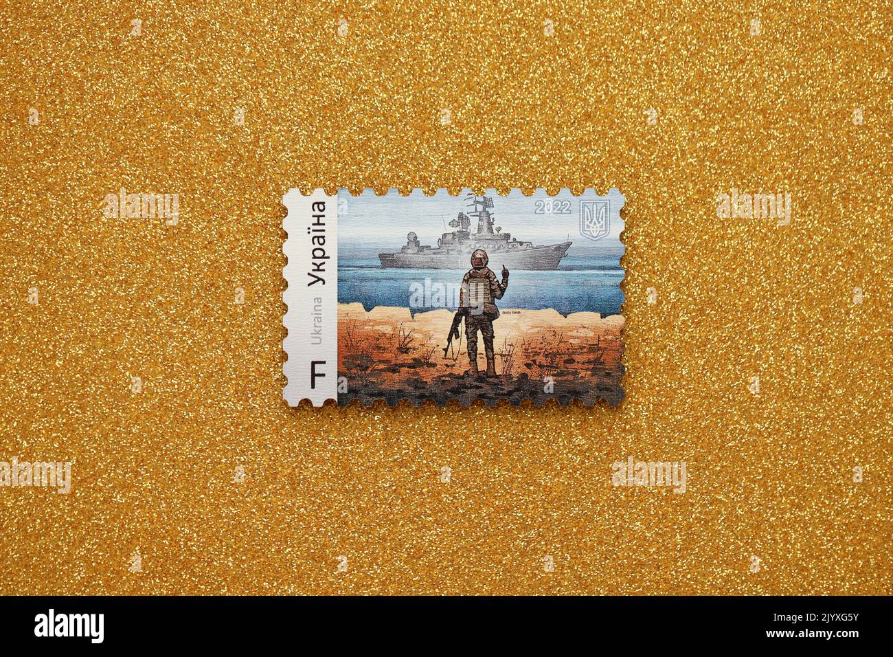 TERNOPIL, UKRAINE - SEPTEMBER 2, 2022 Famous Ukrainian postmark with russian warship and ukrainian soldier as wooden souvenir on golden glitter backgr Stock Photo