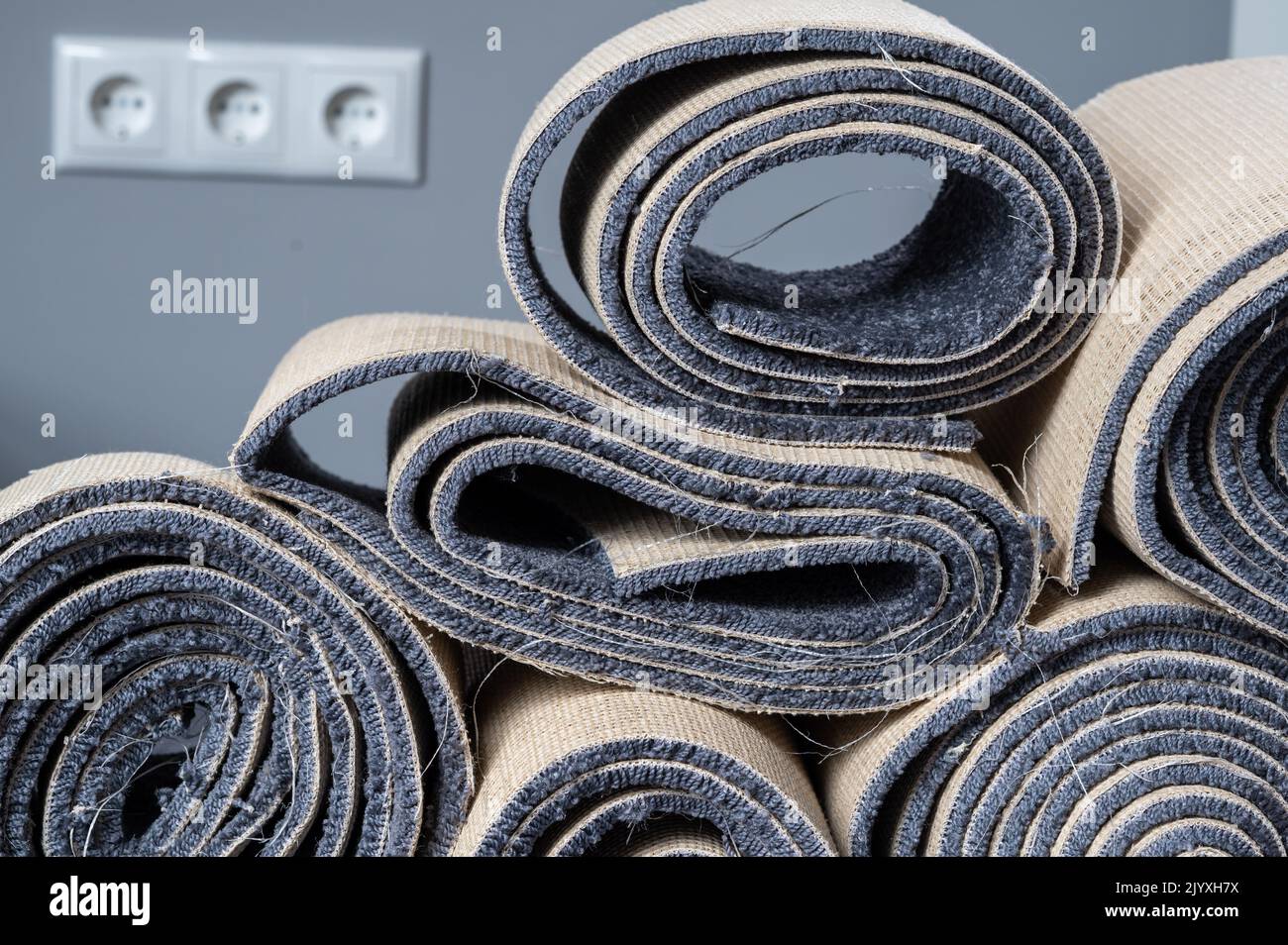 Stacked old carpet rolls in a grey room. Stock Photo