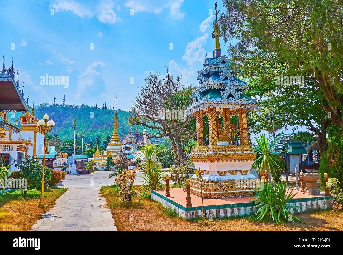 The tall golden Chedi of Wat Chong Klang Temple, topped with hti umbrella is seen behind the garden and mondop shrine of Wat Chong Kham Temple, Mae Ho Stock Photo
