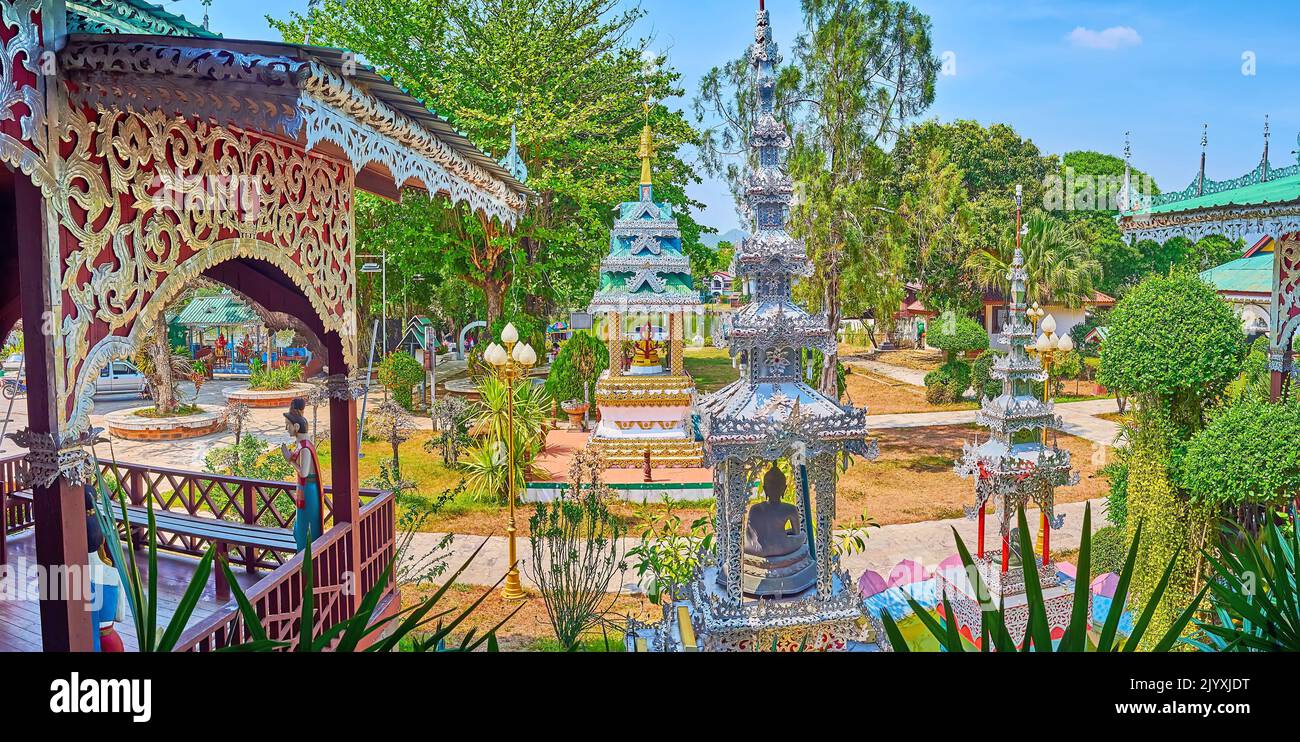 The lush tropical garden of Wat Chong Kham Temple with ornate silver mondop shrines with carved pyathat (multi-tired) roofs, Mae Hong Son, Thailand Stock Photo