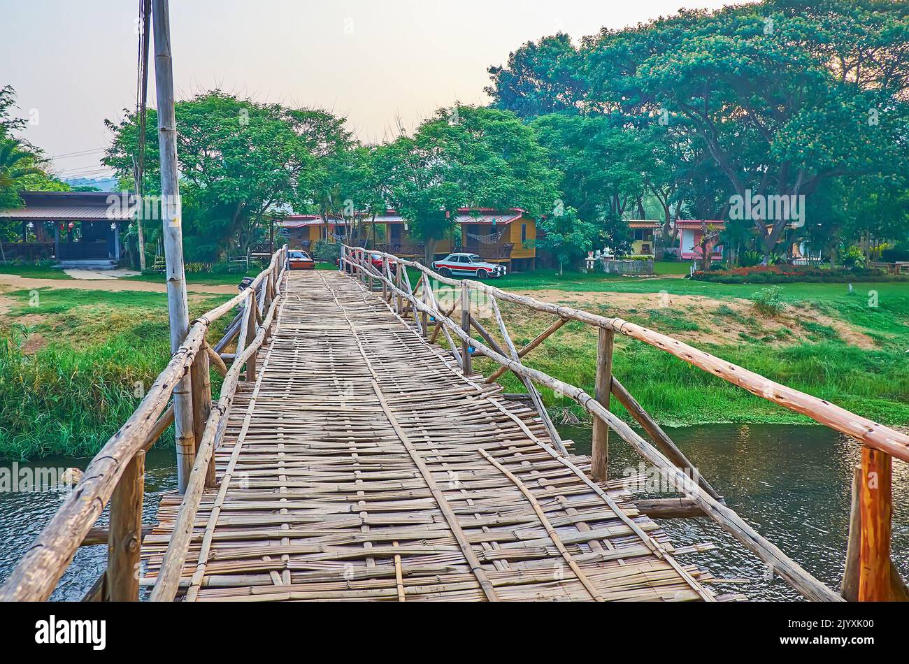 Walk down the shabby bamboo bridge across Pai River, surrounded with lush greenery, Pai, Thailand Stock Photo