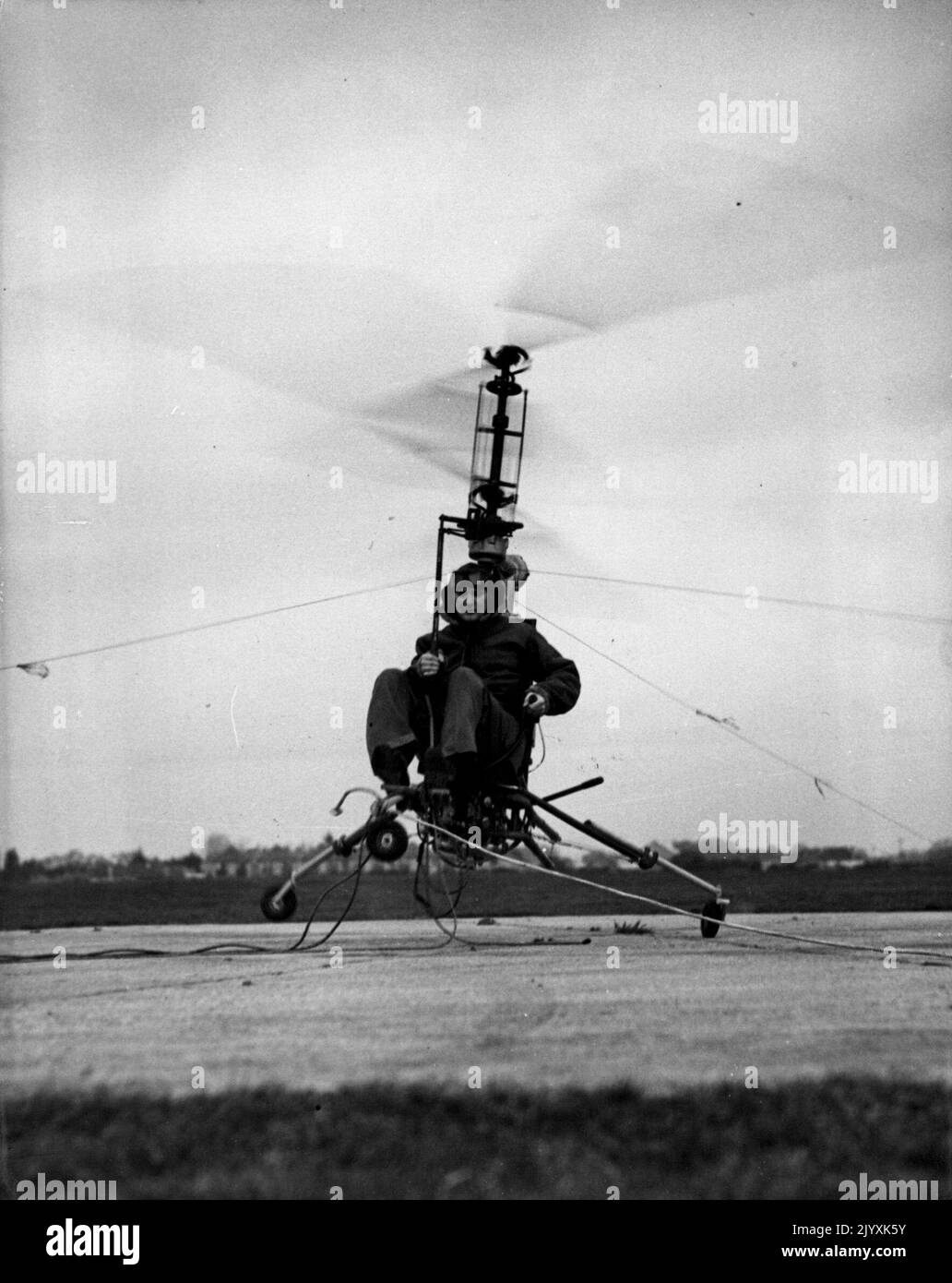 Flying Motor-Cycle Tames The Air -- The 'Hoppicopter' motor-cycle of the air, took the air - in a very small dose - in its first engine tests at Somerford Aerodrome, Christchurch, Hampshire. The 'Hoppicopter' based on the machine designed by the American, H.T. Pentecost, was airborne for only a few minutes, for it was tethered by steel cables. Mr. Berry Martin, managing director of the Winton (Hampshire) factory that built the midget flying machine, piloted it on its first hop. December 12, 1949. Stock Photo