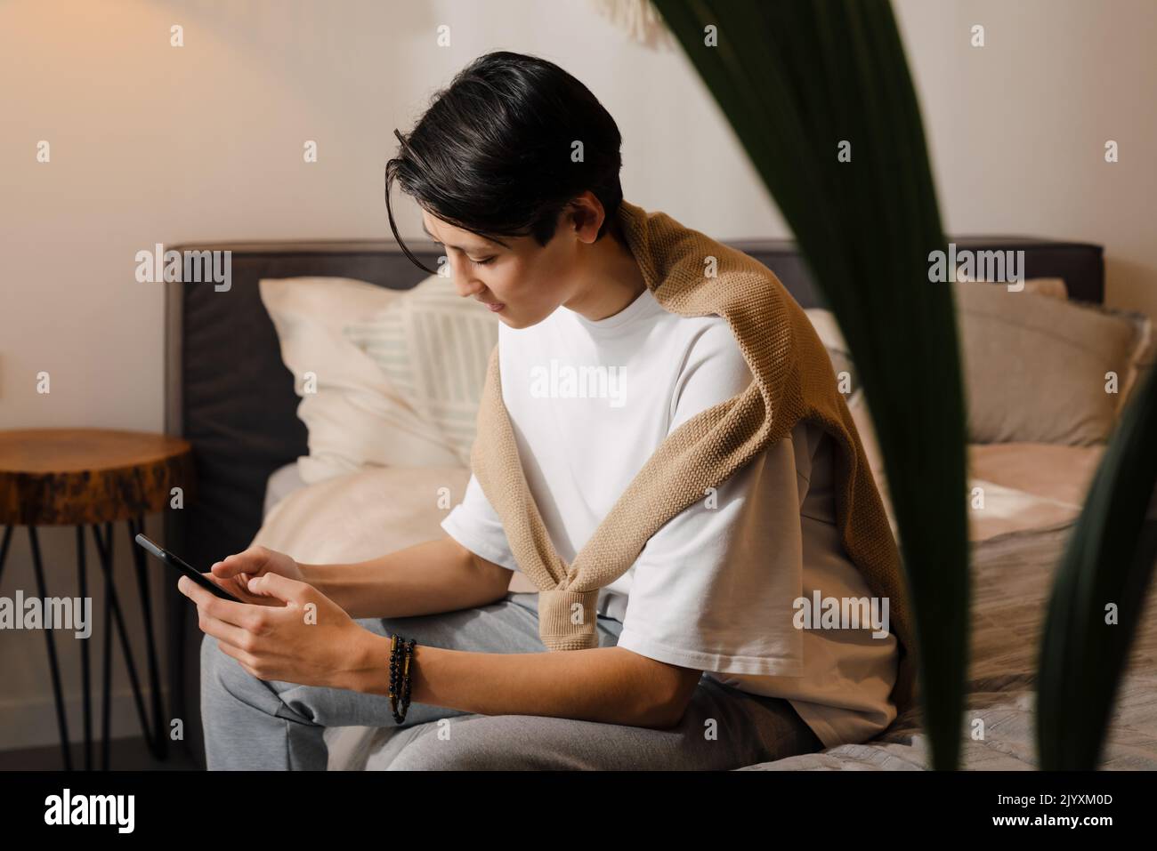 Asian boy using mobile phone while sitting on bed at home Stock Photo