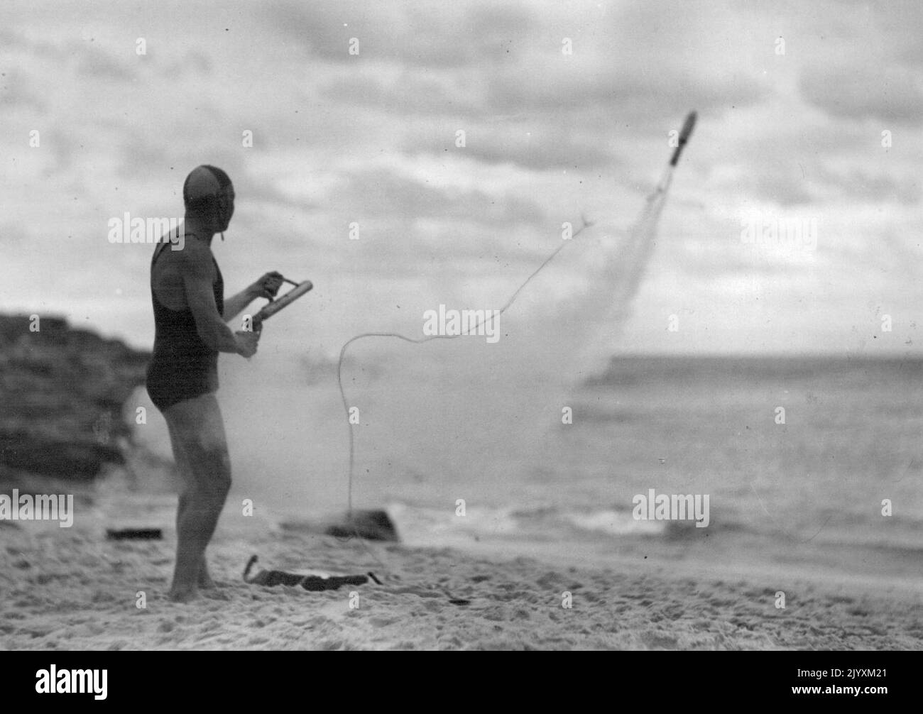 This is the rocket at the start of its run. The orange colored, buoyant line attached to it can be seen spinning out of a box at the firer's feet. A tiny, transparent dome on the rocket's nose houses an electric light bulb which can be lit for night rescues. Sydney surf clubs found these rockets too dangerous in rescue work. They could not be fired accurately enough. July 06, 1947. Stock Photo