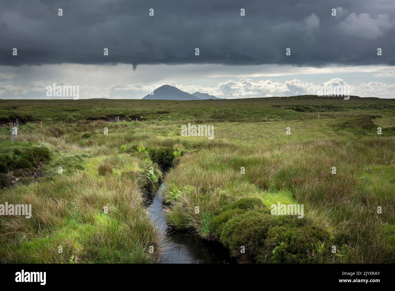 The vast peat landscape of county Mayo in Ireland, with Slievemore on Achill Island on the horizon. Dark clouds gather over the green landscape Stock Photo
