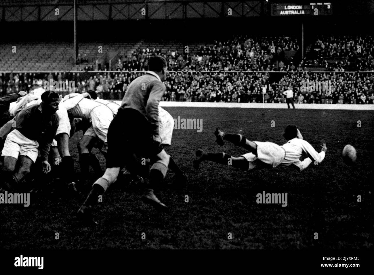 Holiday Rugby -- P. W. Sykes, London's scrum-half, makes a speedy dive and gets the ball away from a scrum break-up to his forward line. Australians meet London Counties at Twickenham, London. Dive Pass. London Counties half-back P. W. Sykes dives as he shoots the ball to a support. Plunging forward in the dark pants is the referee. London Counties won. December 26, 1947. (Photo by Sport & General Press Agency Limited). Stock Photo
