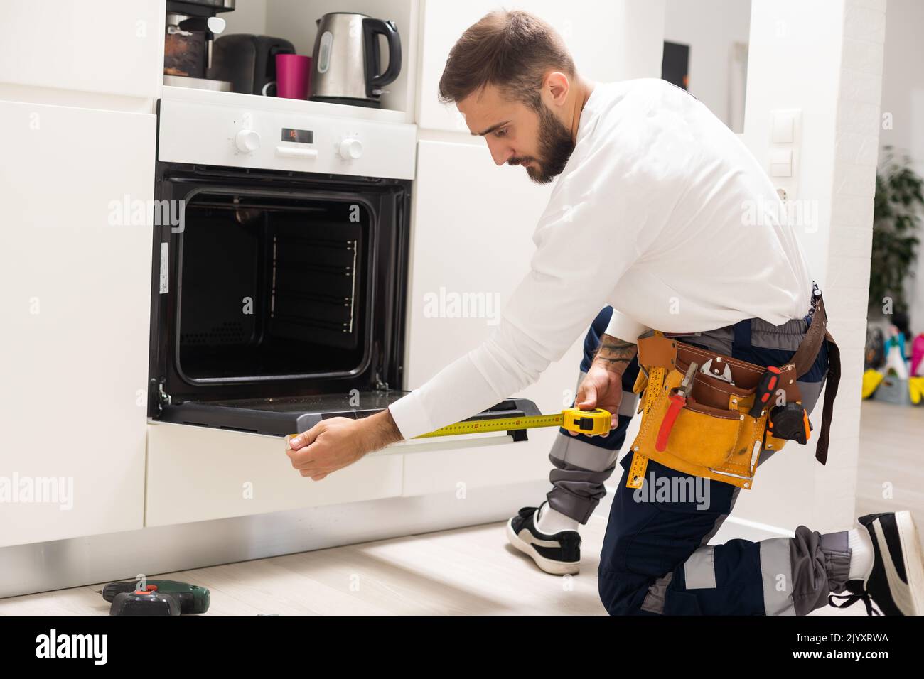 Young Male Technician Repairing Oven In Kitchen Stock Photo