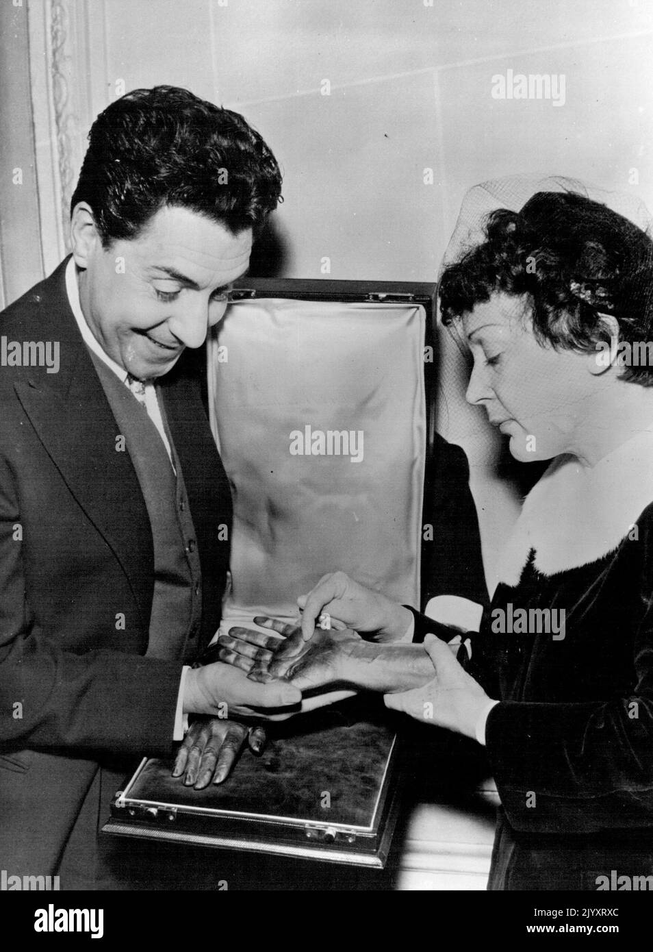 A Hand In Celebration -- Edith Piaf with husband Jacques Pills as they admire their unusual Anniversary gift. Singer Edith Piaf Celebrated Her first wedding anniversary in Paris yesterday. At the Champs-Elysees Pavilion Edith was Presented a Bronze cast of her hands. The presentation was made by the her recording company. The Bronze hands were made by the Chiroteque Francais. January 5, 1954. (Photo by Paul Popper, Paul Popper Ltd.). Stock Photo