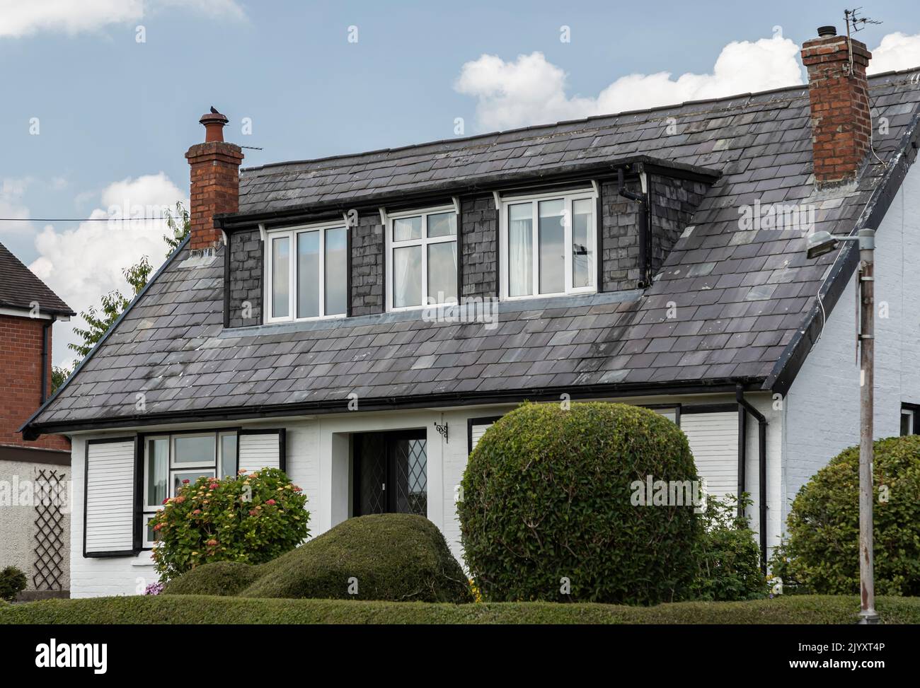 Darnhall, Cheshire, UK - June 23rd, 2022 - Bungalow with slate roof and dormer windows against a blue sky with small shrubs in the garden Stock Photo