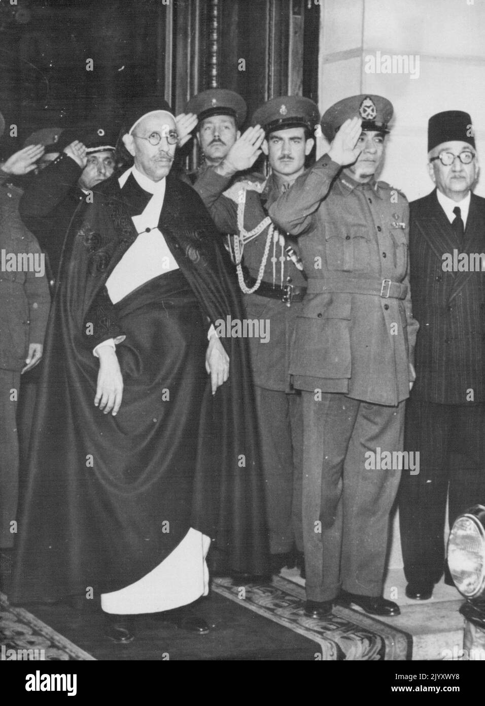 King Idris In Cairo King Idris El Senussi (left), listening to the band playing the Libyan National anthem on his arrival in Cairo, December 2. Let to right, are: King Idriss el Senussi; Prince Ambdel Moneim, The Prince Regent and Premier Mayor General Mohamed Naguib, Person at Extreme right in picture no identified. King Idris Ei Senussi, First Moanrch of Libya, arrived in Cairo December 2 for a week-long state visit. The monarch who travelled from Benghazi Eastwards by car and Rail, was greeted on arrival in Cairo railway station by Egypt's Regent Prince Abdel Moneim' Premier Major general M Stock Photo