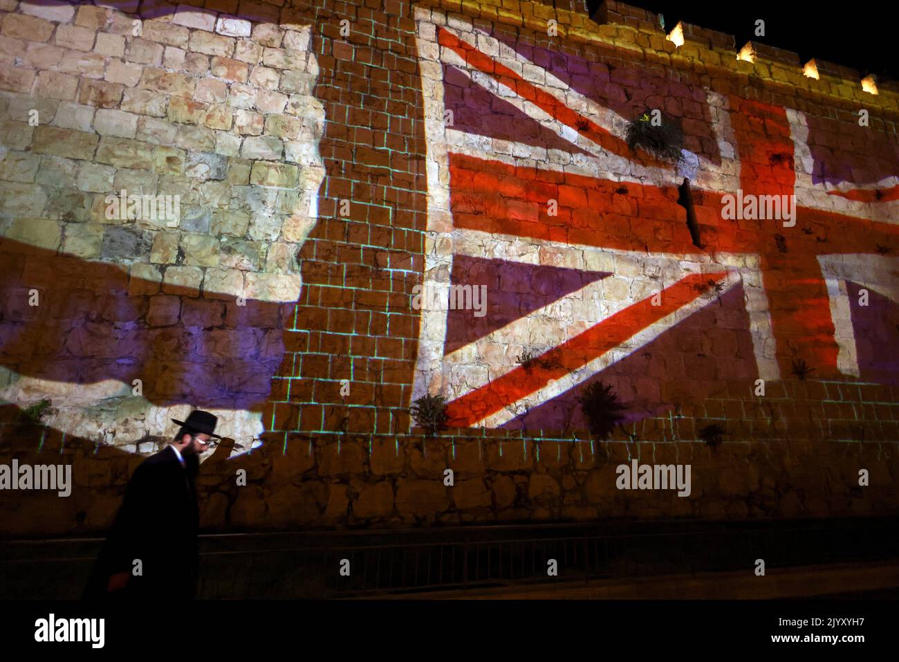An Ultra Orthodox Jewish man walks by walls of Jerusalem's Old City as it is illuminated with the Union Jack flag following the death of Queen Elizabeth, Britain's longest-reigning monarch, in Jerusalem September 8, 2022. REUTERS/Ronen Zvulun Stock Photo