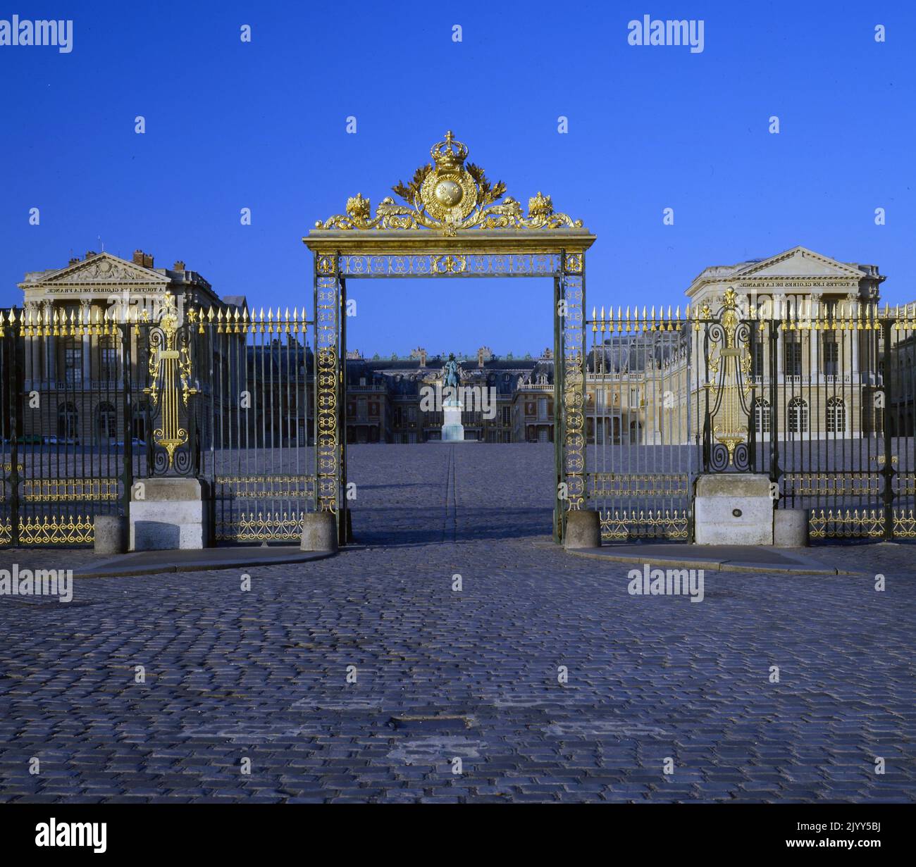 Gilded gates to the Palace of Versailles. Versailles was a royal chateau in the Ile-de-France region of France. Versailles was the seat of political power in the Kingdom of France from 1682, when King Louis XIV moved the royal court from Paris, until the royal family was forced to return to the capital in October 1789, within three months after the beginning of the French Revolution Stock Photo
