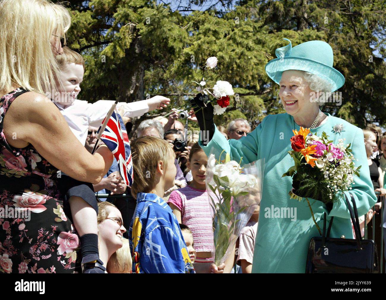 Queen Elizabeth II receives flowers from Isaac Dodd, 2, in the arms of ...