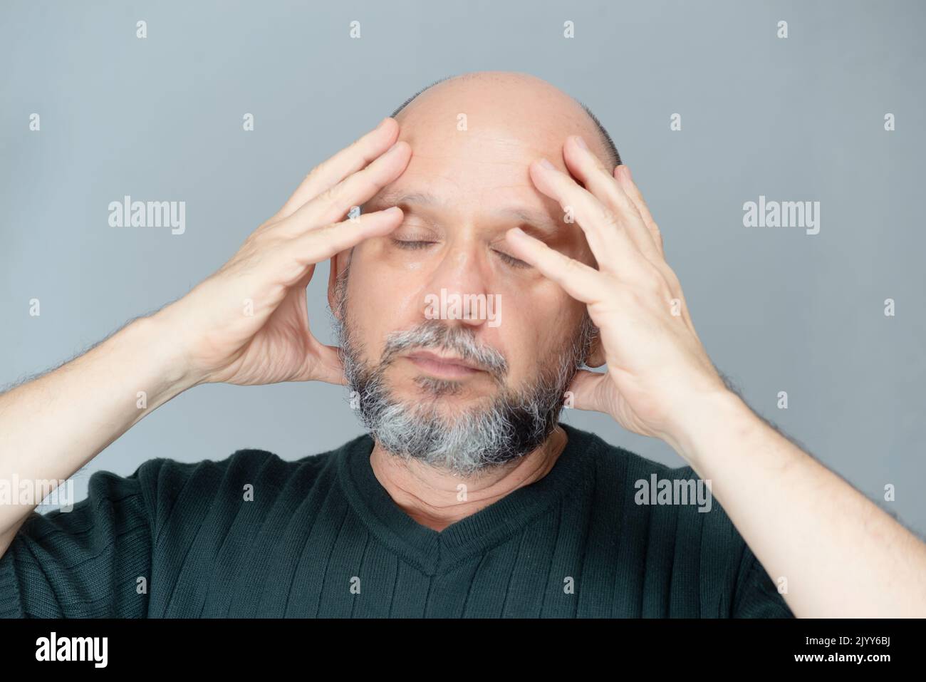 Portrait of mature man standing on light background. Bearded bald man with hands on his face. Formal style. Stock Photo