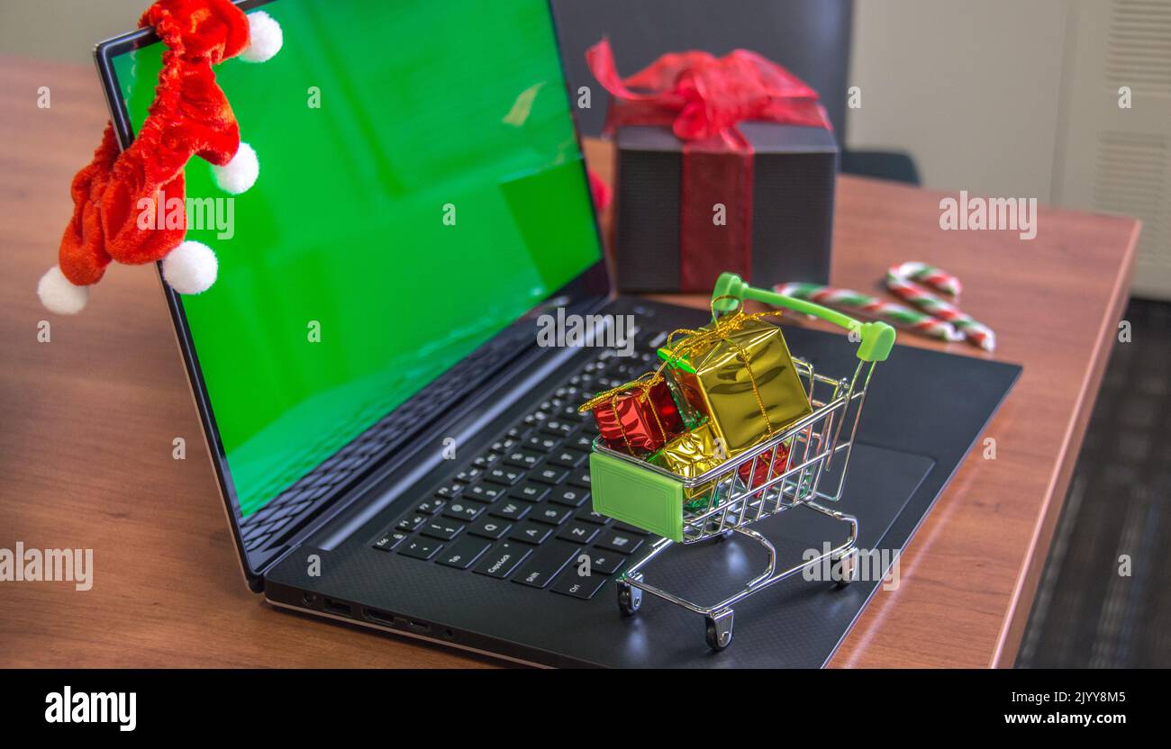 Shopping cart full of christmas gifts on laptop computer with green screen. Online holiday shopping, e-commerce and worldwide shipping concept. Mockup Stock Photo