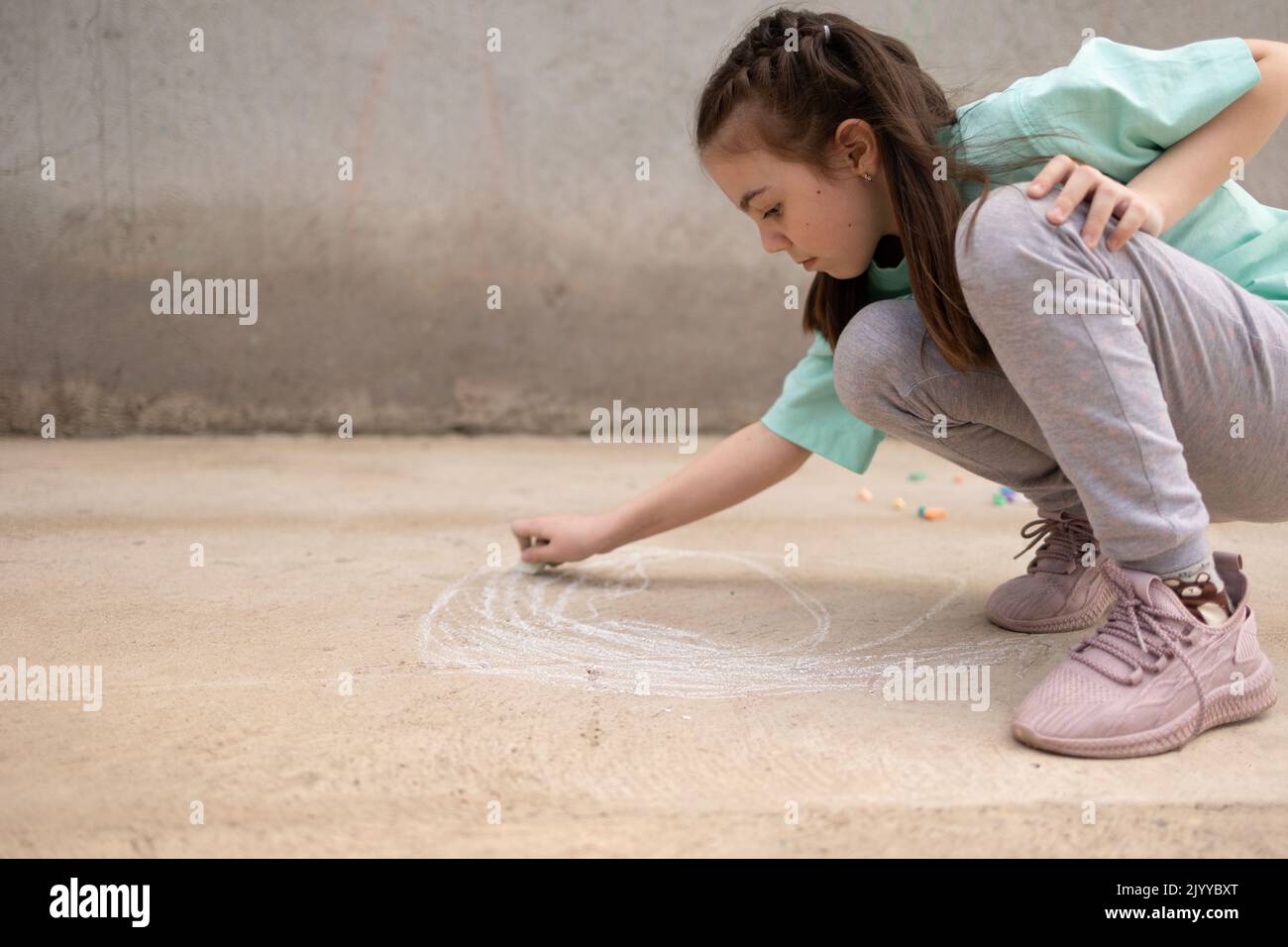 Girl draws with colorful crayons on pavement. Children's drawings with chalk on wall. Creative kid. Joy of childhood. High quality photo Stock Photo