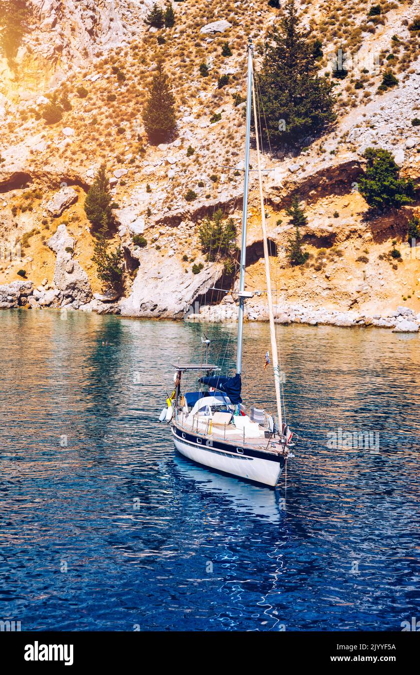 Yacht anchoring in crystal clear turquoise water in front of the tropical island, alternative lifestyle, living on a boat. View of yacht at anchor on Stock Photo