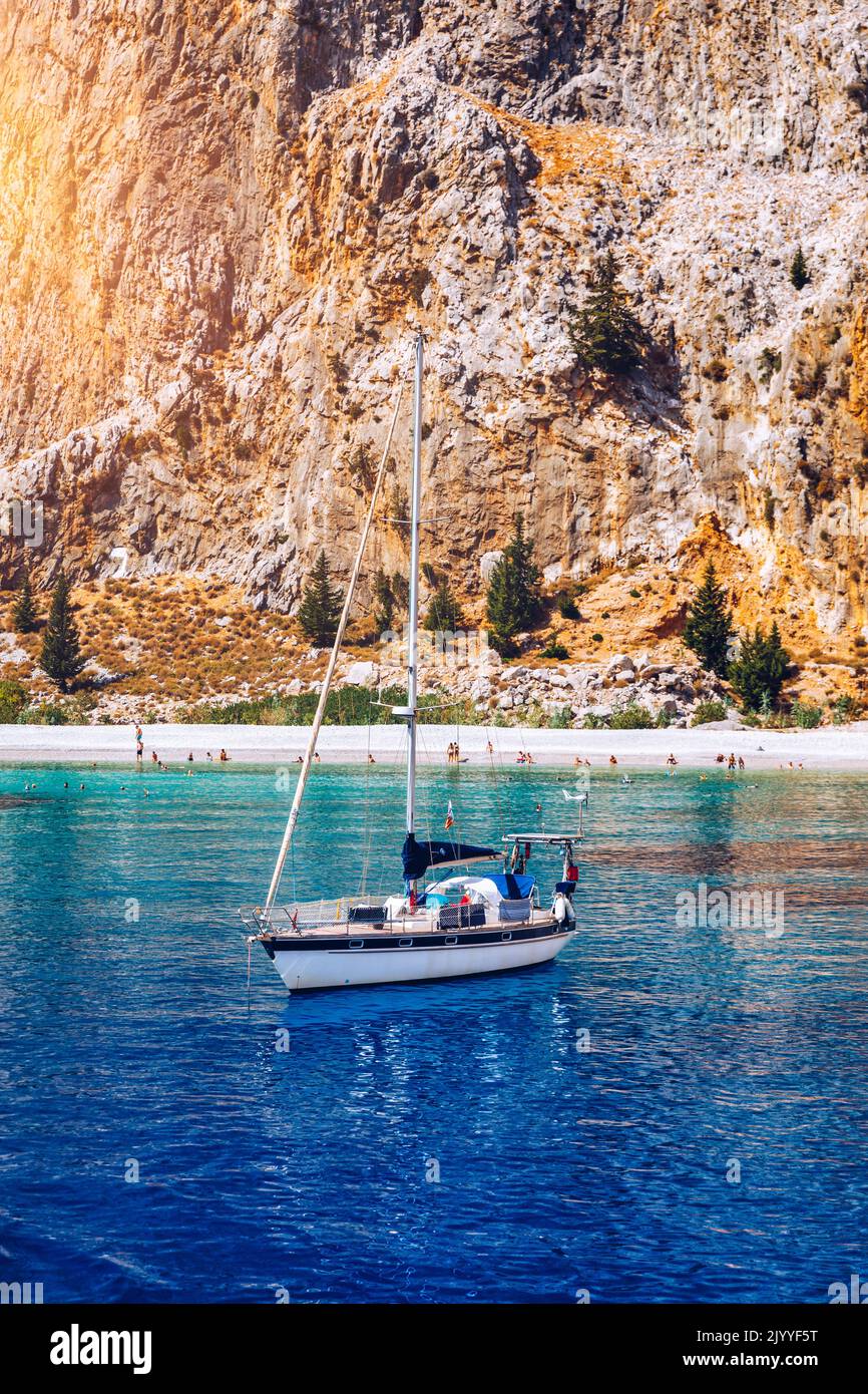 Yacht anchoring in crystal clear turquoise water in front of the tropical island, alternative lifestyle, living on a boat. View of yacht at anchor on Stock Photo