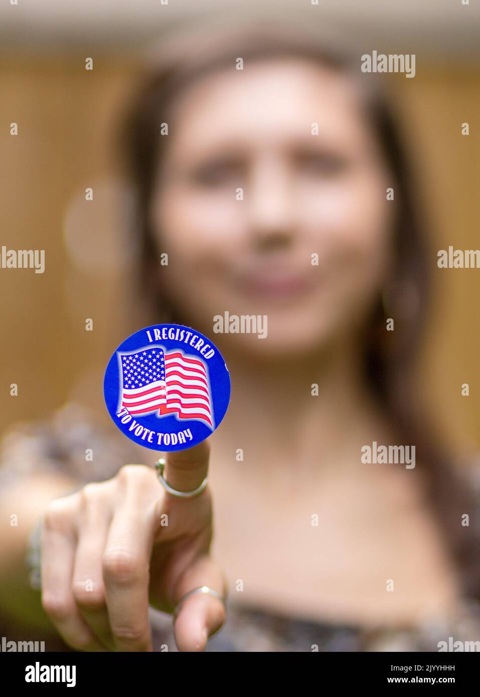 A young woman in shallow depth of field holds up a sticker saying 'I registered to vote.' Stock Photo