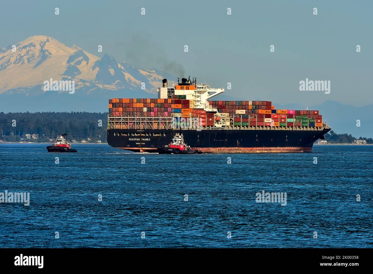 An ocean going ship with a load of bulk containers gets escorted by two tug boats into the
