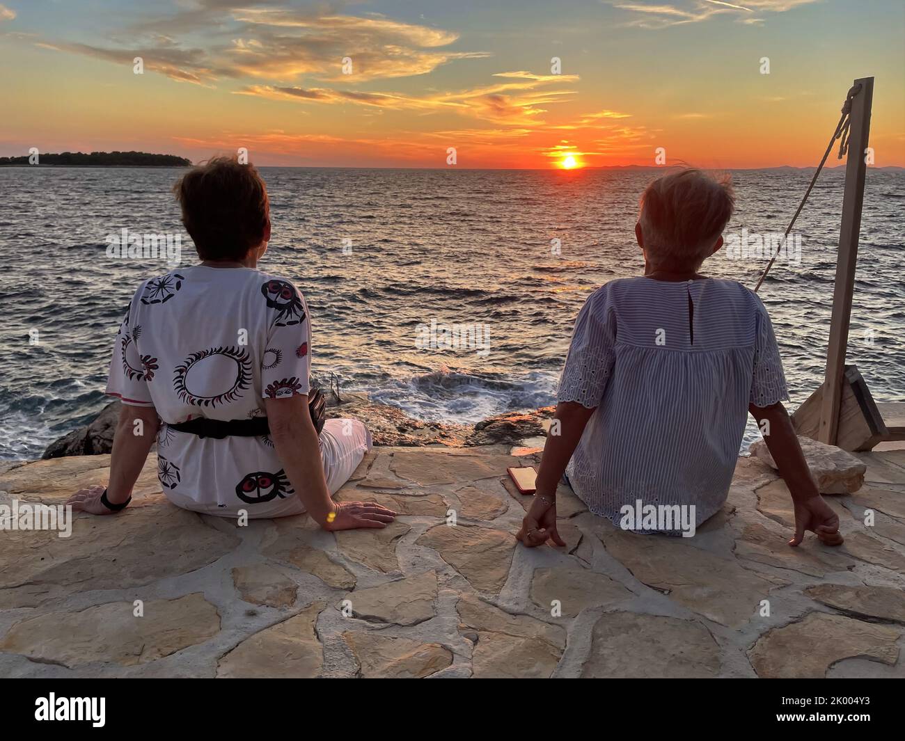 Two senior women sitting on the sea shore during sunset Stock Photo