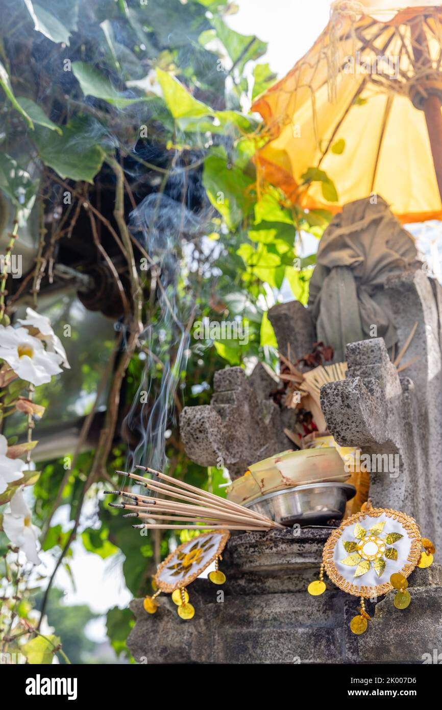 Balinese Hindu altar with yellow umbrella, offerings and burning incense. Bali, Indonesia, Stock Photo