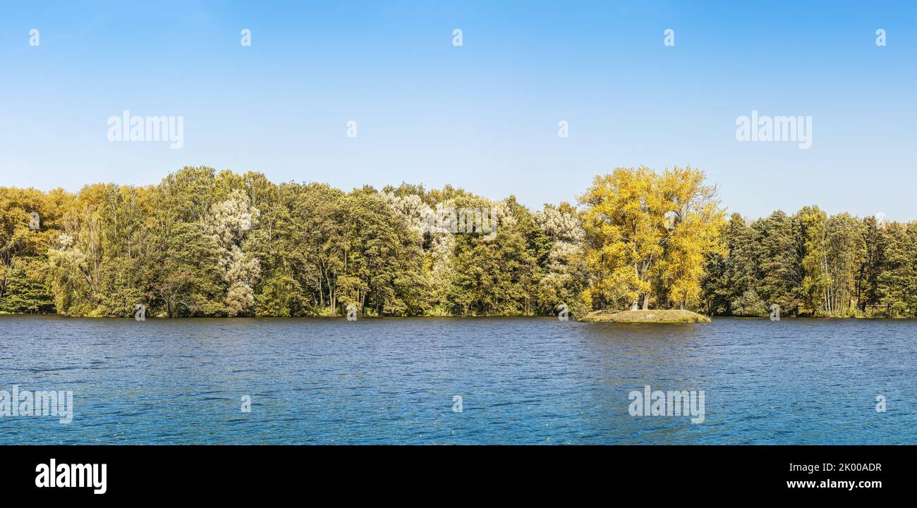 autumn forest on the river shore. panoramic landscape with blue sky and colorful trees. Stock Photo