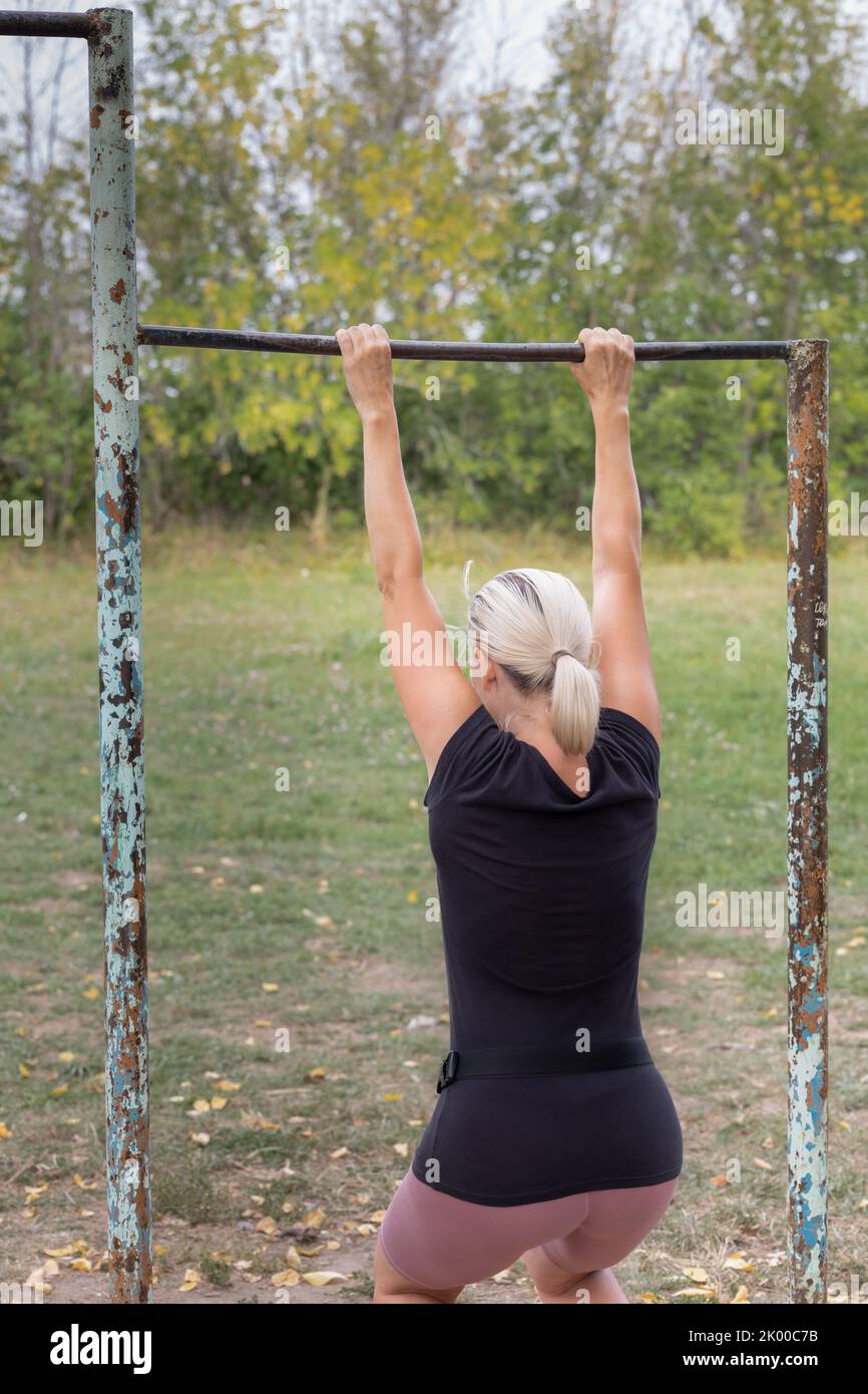girl hanging on the crossbar on the sports ground. Woman hanging on a