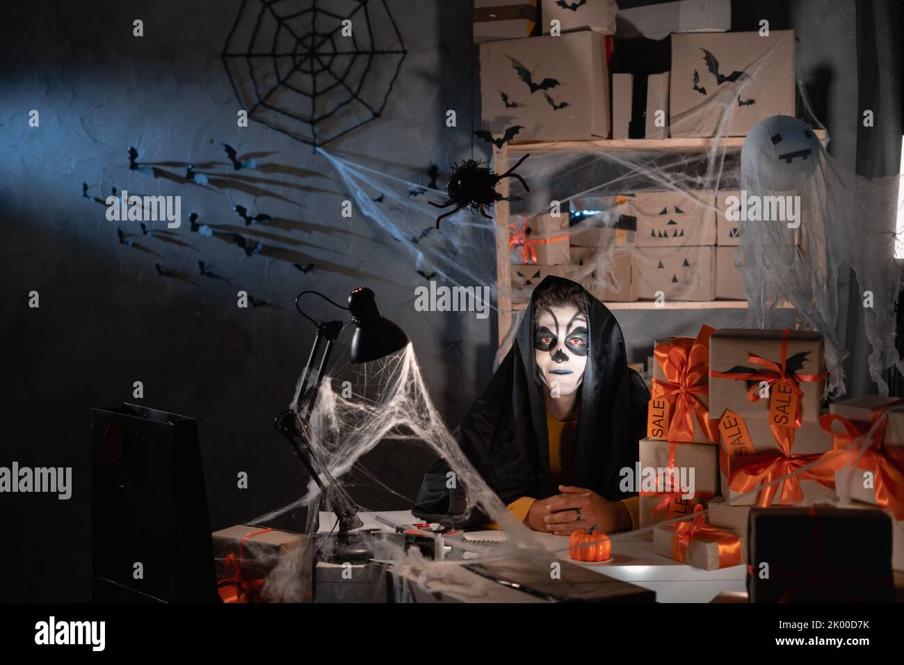 Small and medium business start-up entrepreneur, male entrepreneur with skull make-up sits among boxes with cobwebs. Big sale concept for halloween Stock Photo
