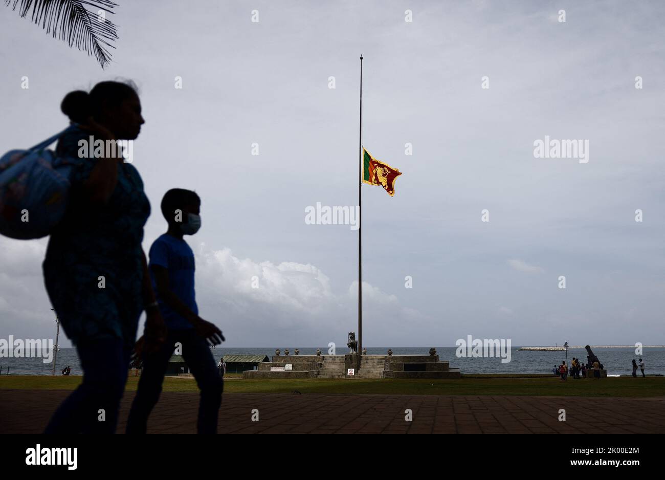 A family walks along a path as Sri Lankan national flag flies at half
