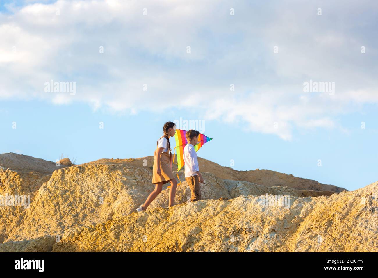Children boy and girl with kite in their hands climb a high mountain. Stock Photo