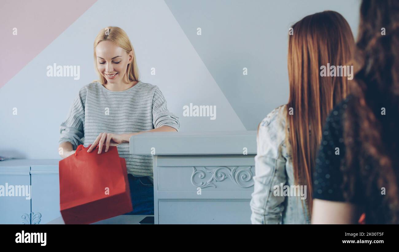 Friendly female cashier is taking garment from customer standing in