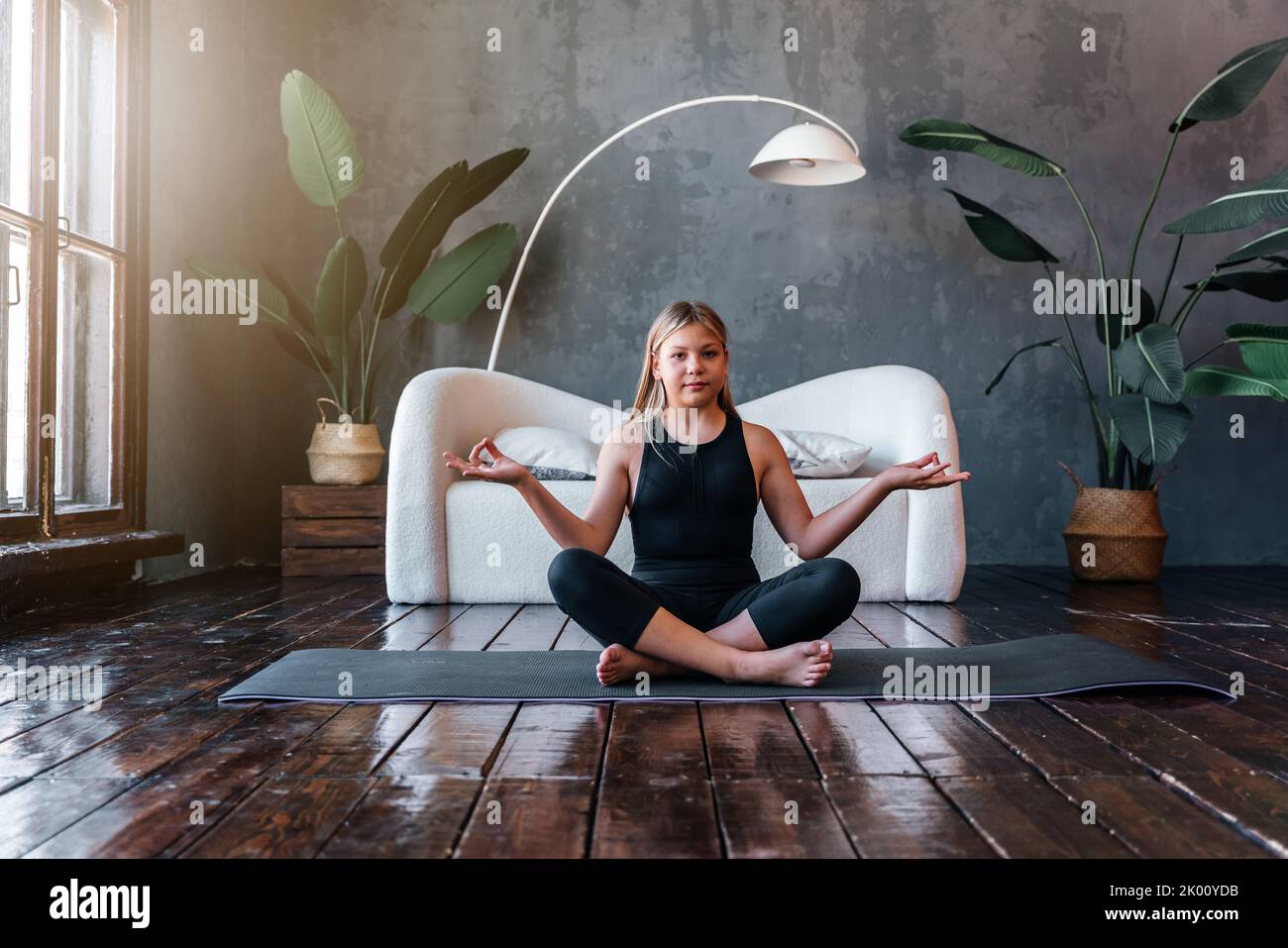 Young attractive girl practicing yoga, sitting in Half Lotus exercise, Ardha Padmasana pose, exercising, meditation session, home interior. High quali Stock Photo