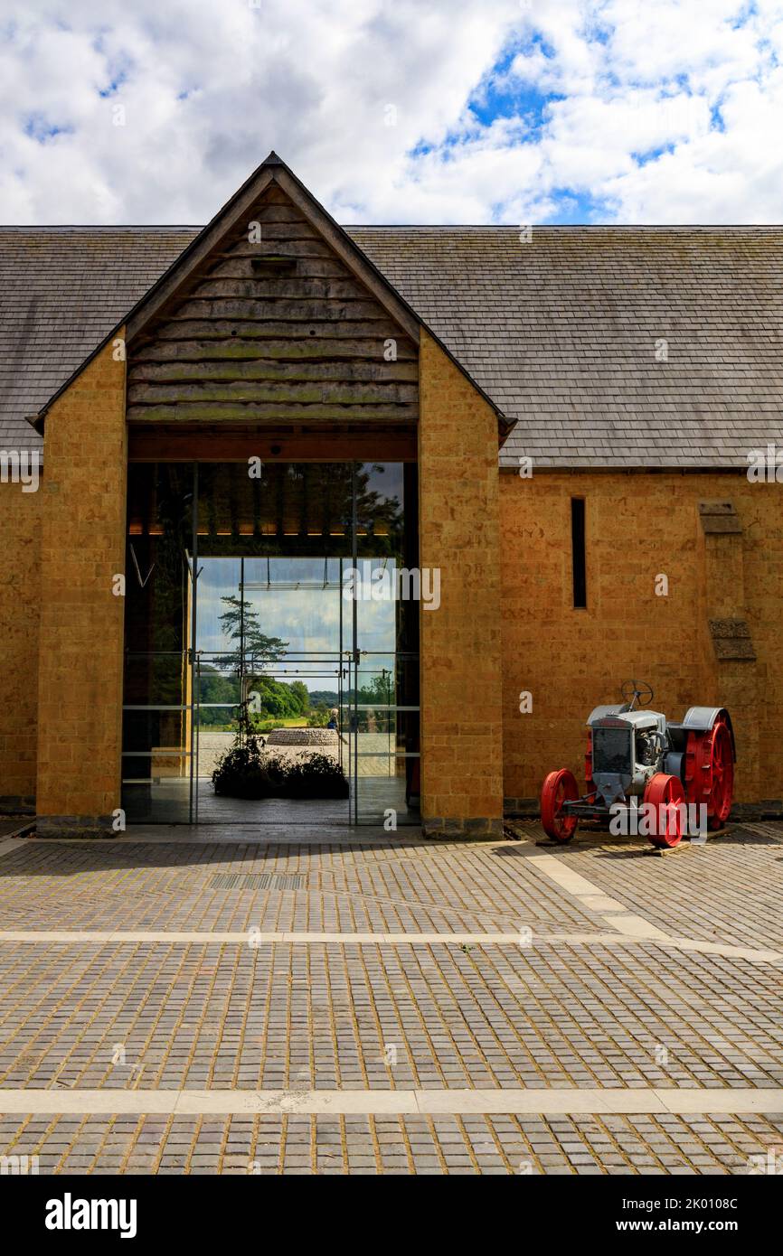 Colourful vintage tractor and farm machinery outside threshing barn at the restored 'The Newt in Somerset' garden and hotel, nr Bruton, England, UK Stock Photo