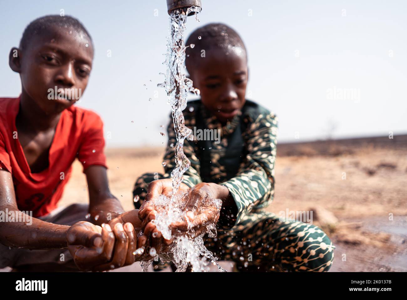 Small malnourished African boys at a village well refreshing themselves; concept of drought, famine and climate change Stock Photo