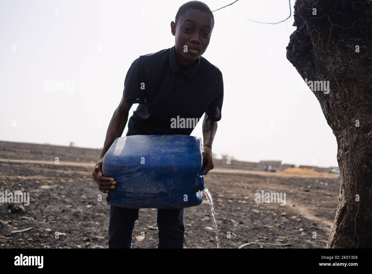 Gloomy and blurry image of a young African man with a can of water, irrigating a dried up field; concept of hopelessness of third world people to cope Stock Photo