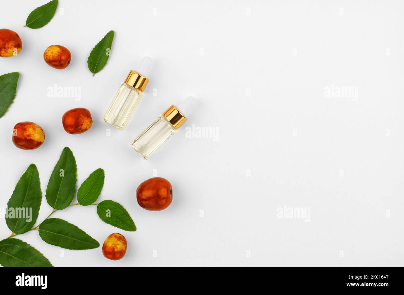 Chinese date fruit and butter, copy space. Jojoba oil in a transparent bottle with a dropper and fresh jojoba fruit on a white background Stock Photo