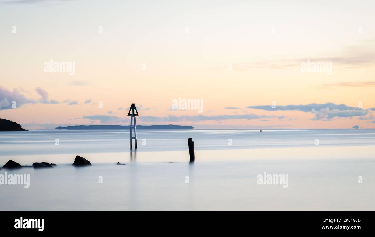 Post and rocks at Milford beach at dawn, Auckland. Stock Photo
