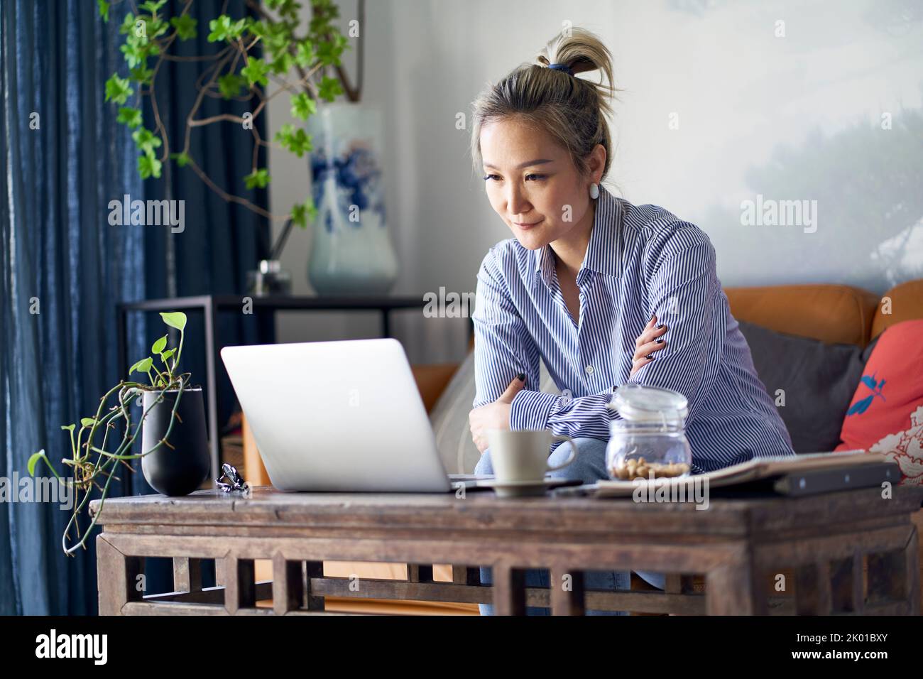 mature professional asian woman working from home sitting in couch looking at laptop computer Stock Photo