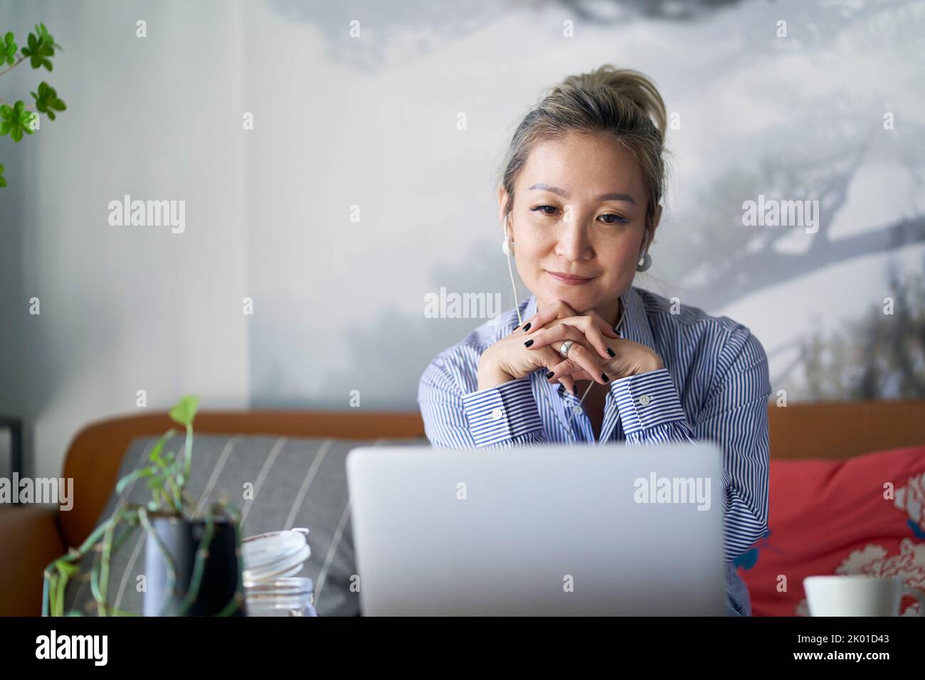 mature professional asian woman working from home sitting in couch looking at laptop computer Stock Photo