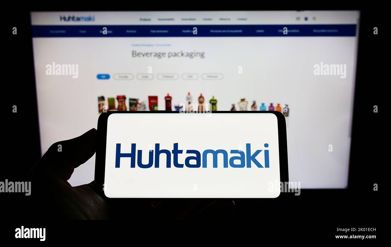 Person holding cellphone with logo of Finnish packaging company Huhtamaki Oyj on screen in front of business webpage. Focus on phone display. Stock Photo