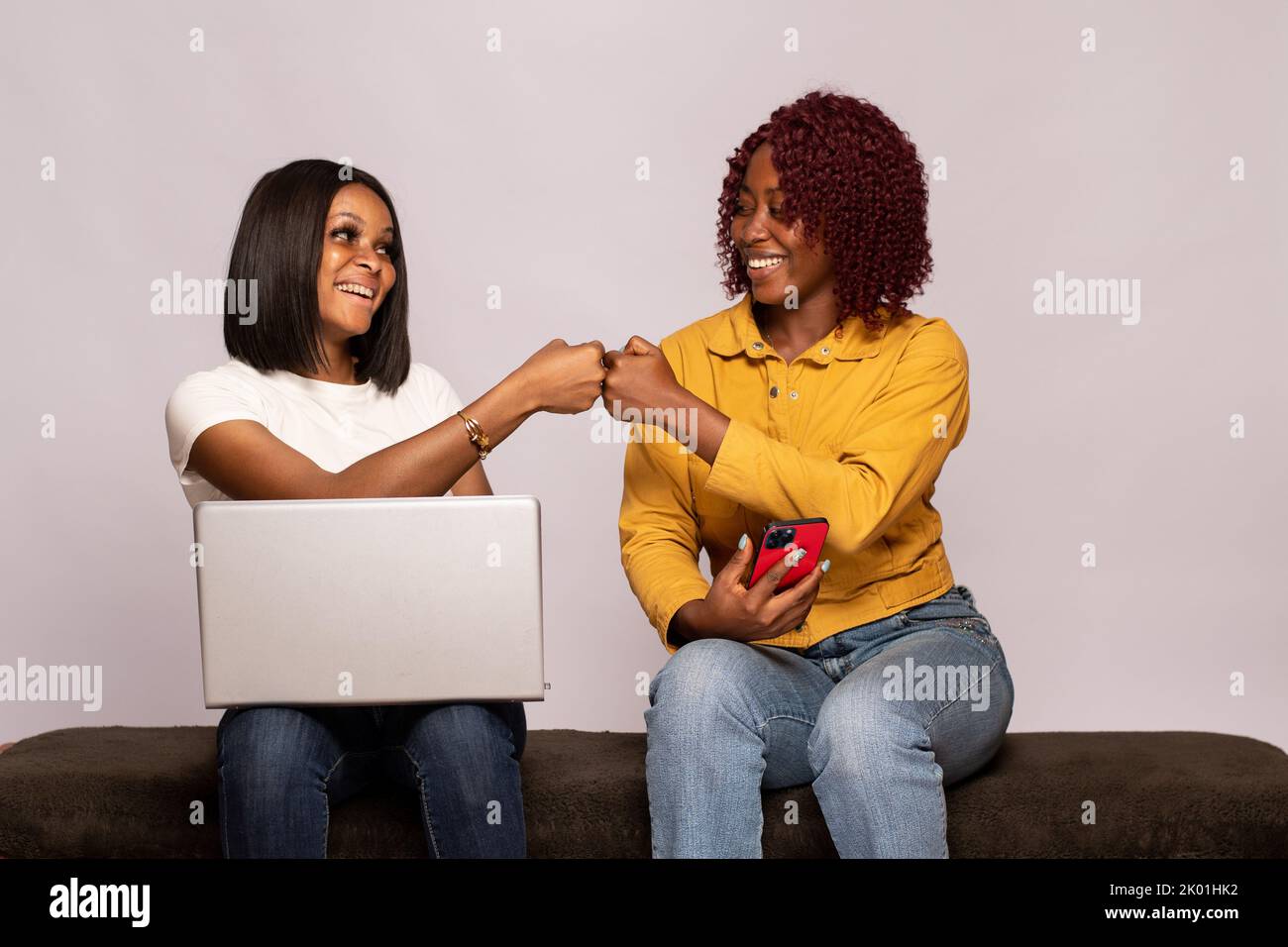 two black girls using their phone and laptop do a fist bump Stock Photo ...