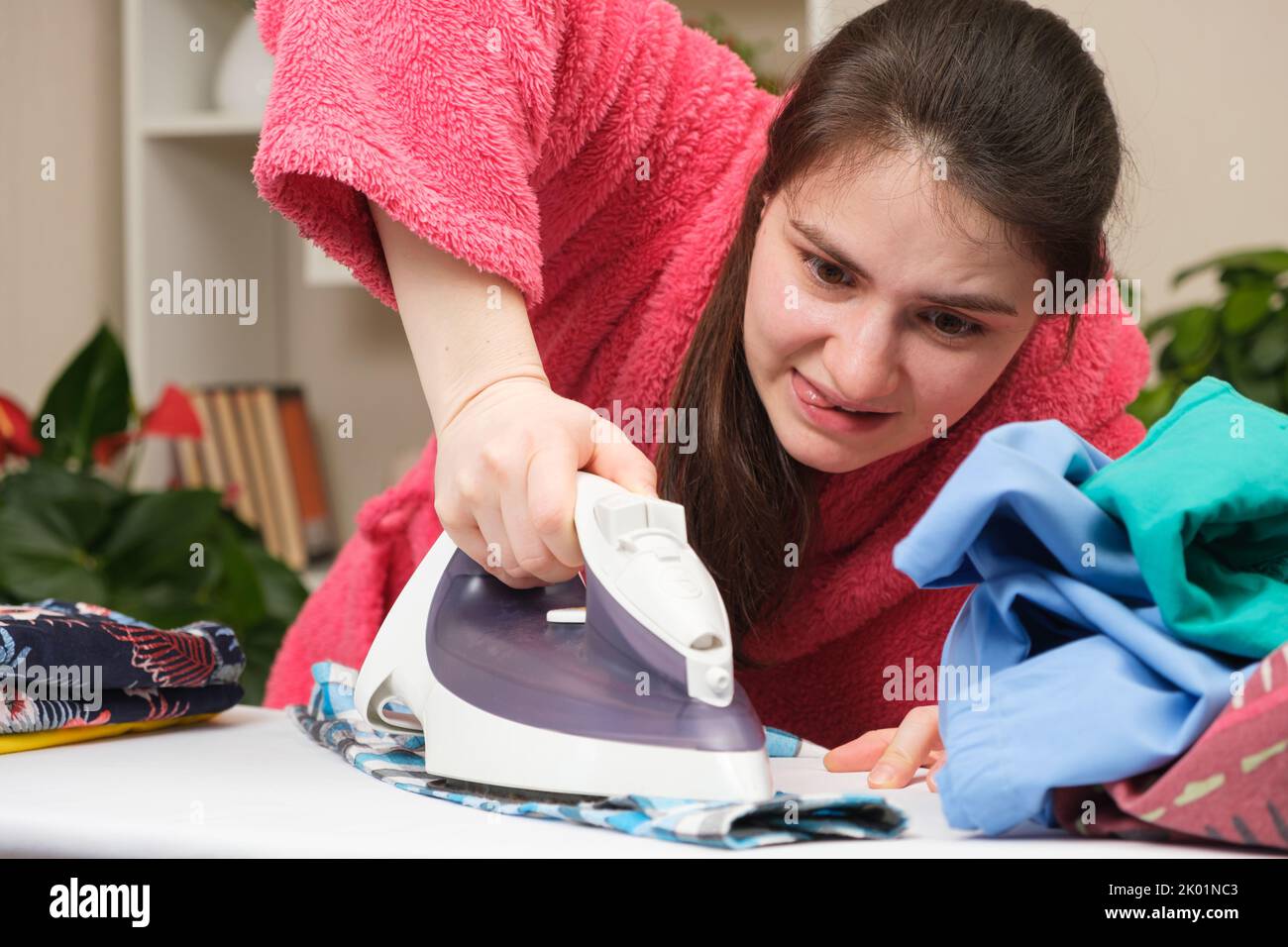A crazy housewife in a pink robe diligently irons clothes with an iron